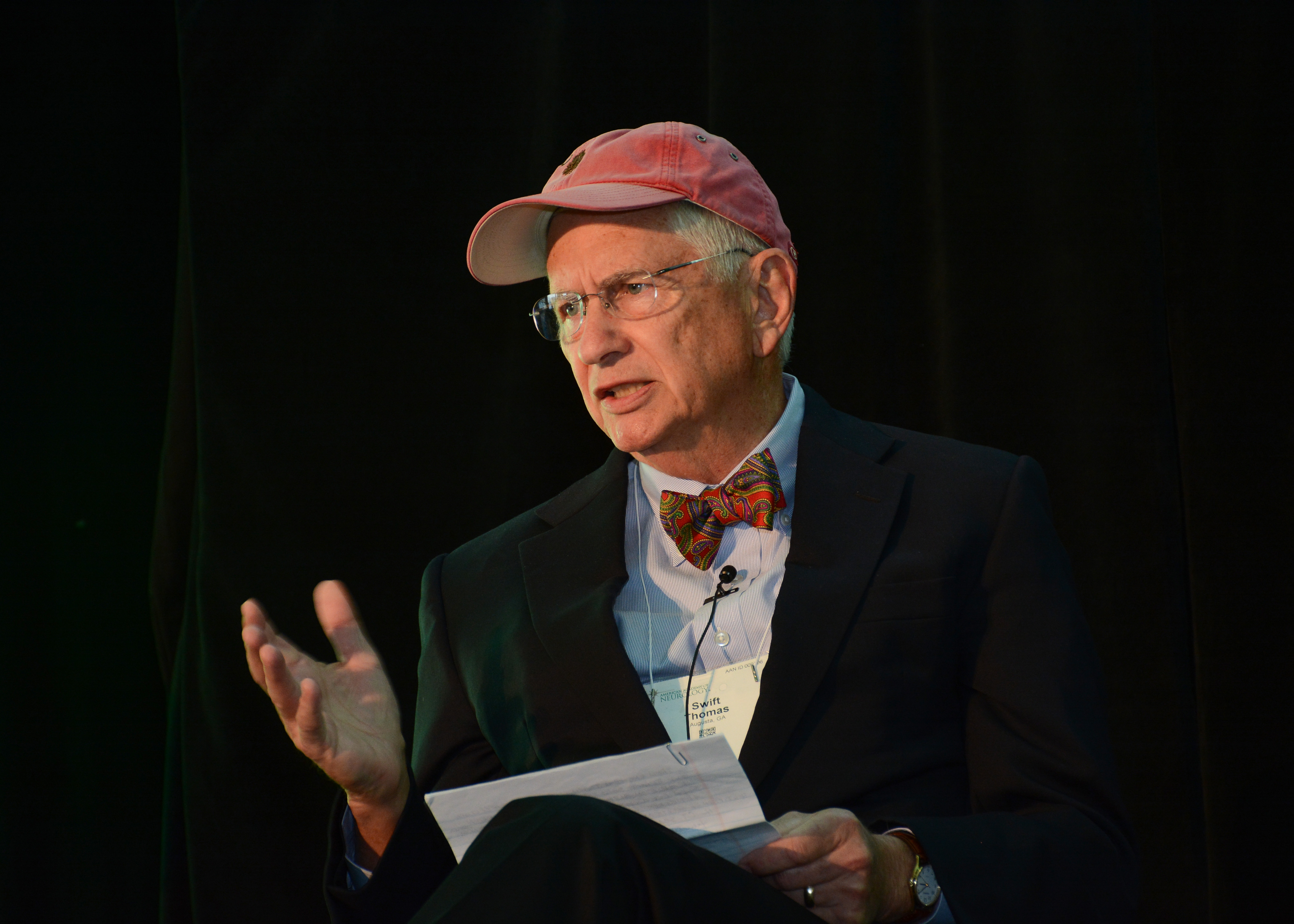 Thomas Swift wearing suit and baseball cap with papers in his lap